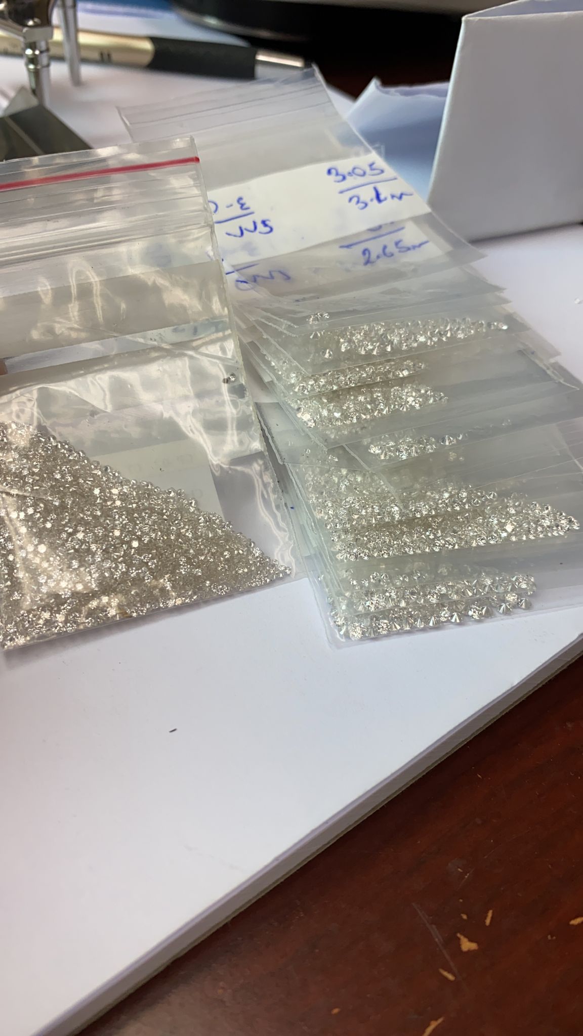 Parcels of loose natural diamonds organized in clear gem bags on a jewelry workbench.