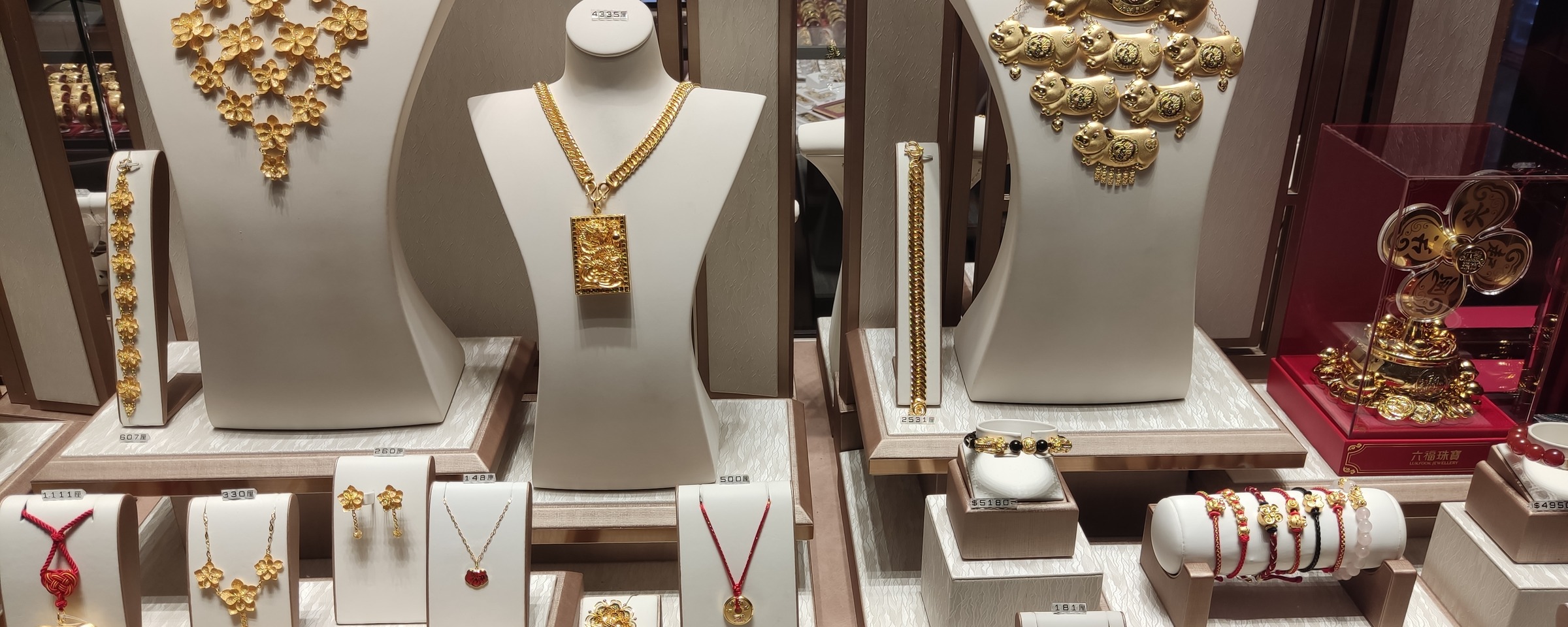 Finished gold necklaces, bangles, bracelets and rings arranged on display busts inside a jewelry store window case.