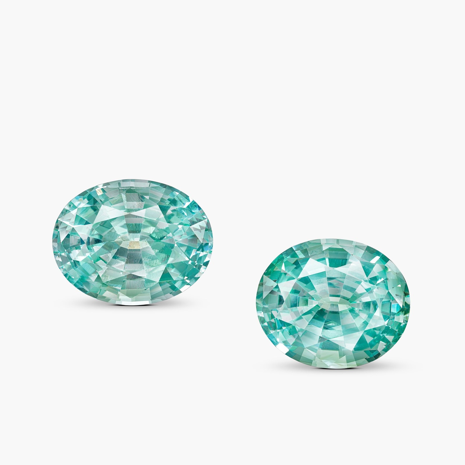 Two large oval Paraiba-type tourmalines with bright blue-green neon color, photographed side by side against a plain pale background.