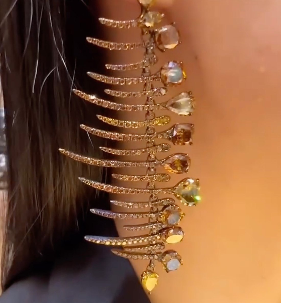 Close view of a Glenn Spiro Fishbone chandelier ear clip with diamond set spines and orange, yellow and near colorless stone drops.