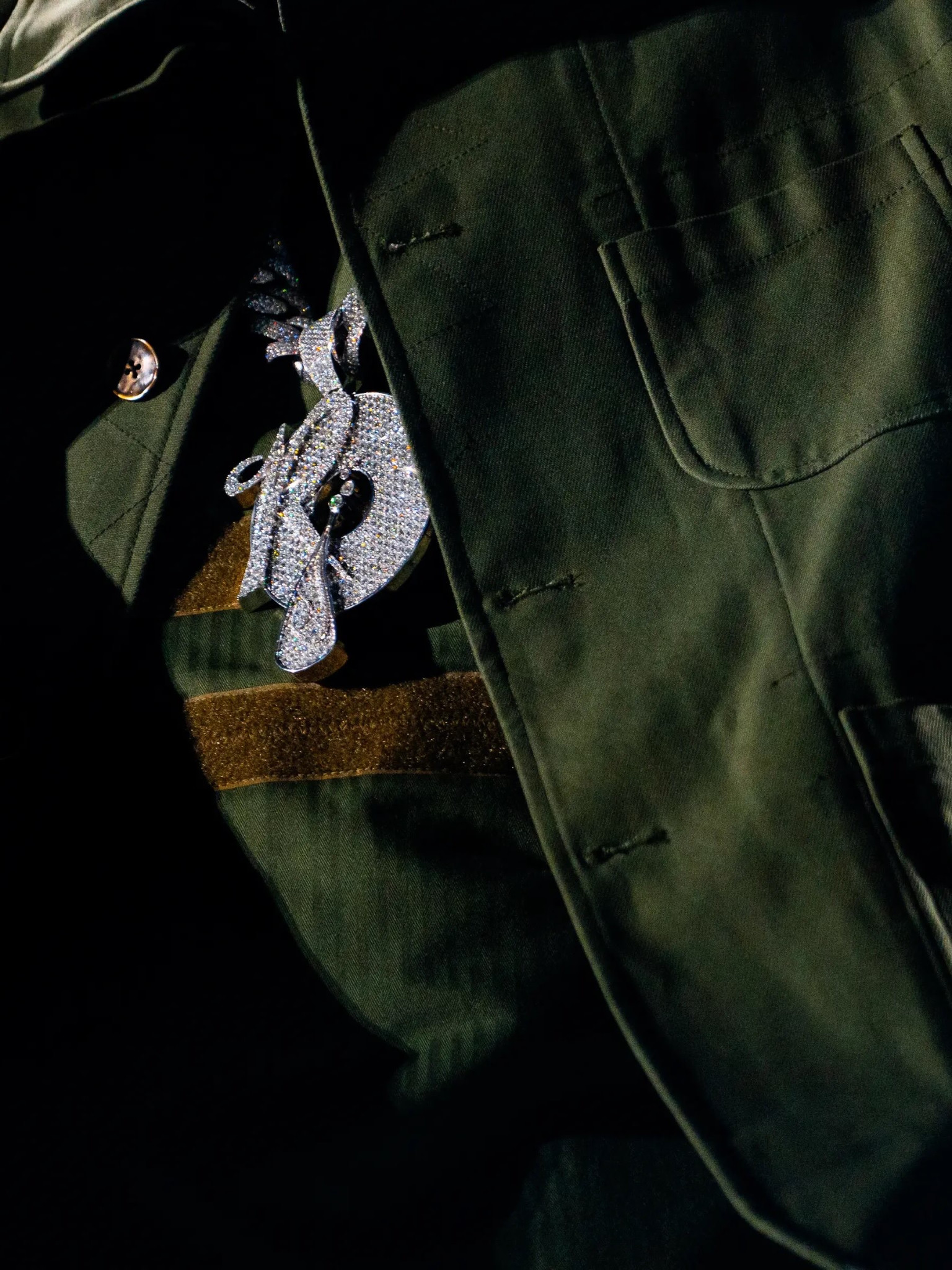 Close-up of a stone-set Roc-A-Fella pendant against olive clothing.