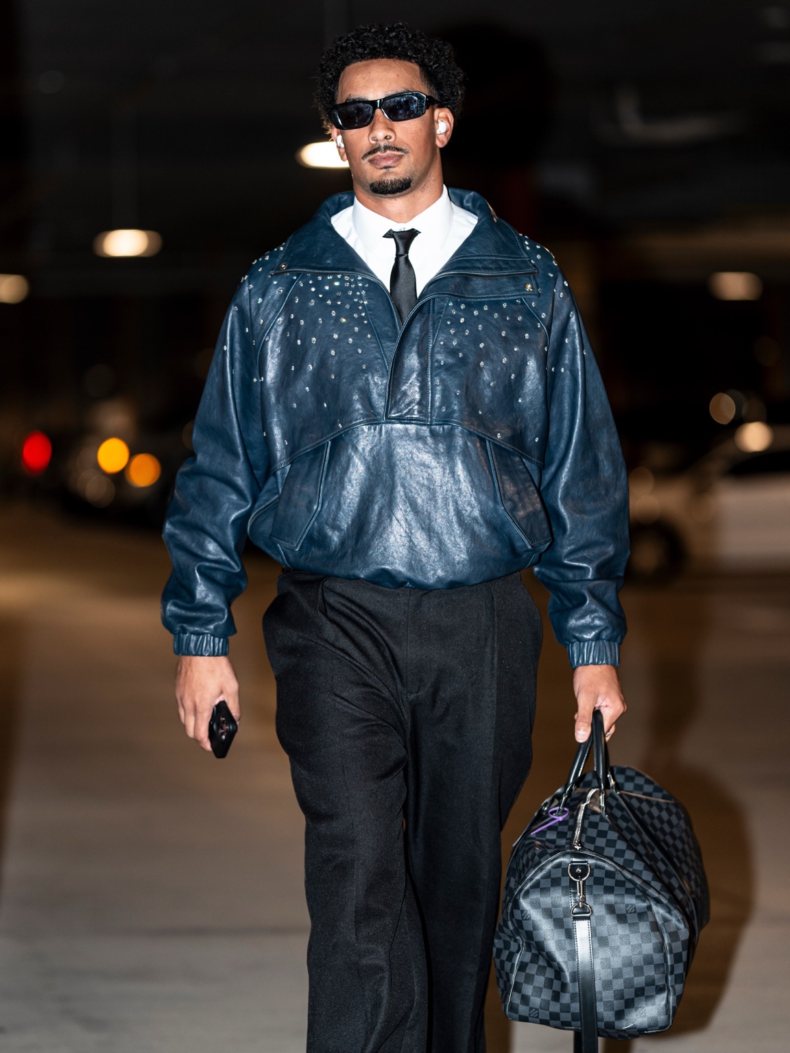 Jordan Love walks into Lambeau Field wearing a midnight blue diamond jacket, black trousers and loafers while carrying a dark duffel bag.